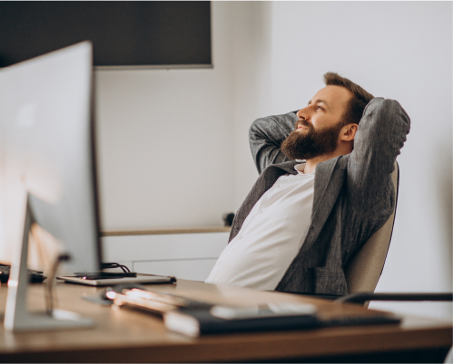 A man holding his hands behind his head and sitting at a computer desk