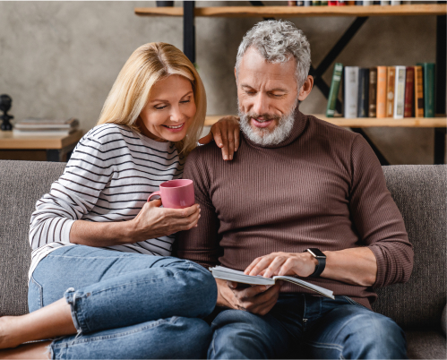 A middle-aged couple sitting on a couch and reading a book